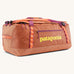 Patagonia black hole 70l duffel bag in bright orange with purple zip details, straps and yellow printed logo on front panel 
