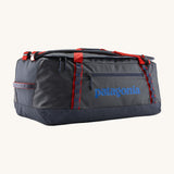 Patagonia black hole 70L duffel bag in smolder blue / amanita red available at Babipur. A dark blue bag with red trim and blue branding on the side. Features shoulders straps and a handle on the top for easy carrying.