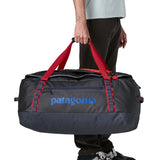 A man carrying the Patagonia black hole 70L duffel bag in smolder blue / amanita red available at Babipur. 