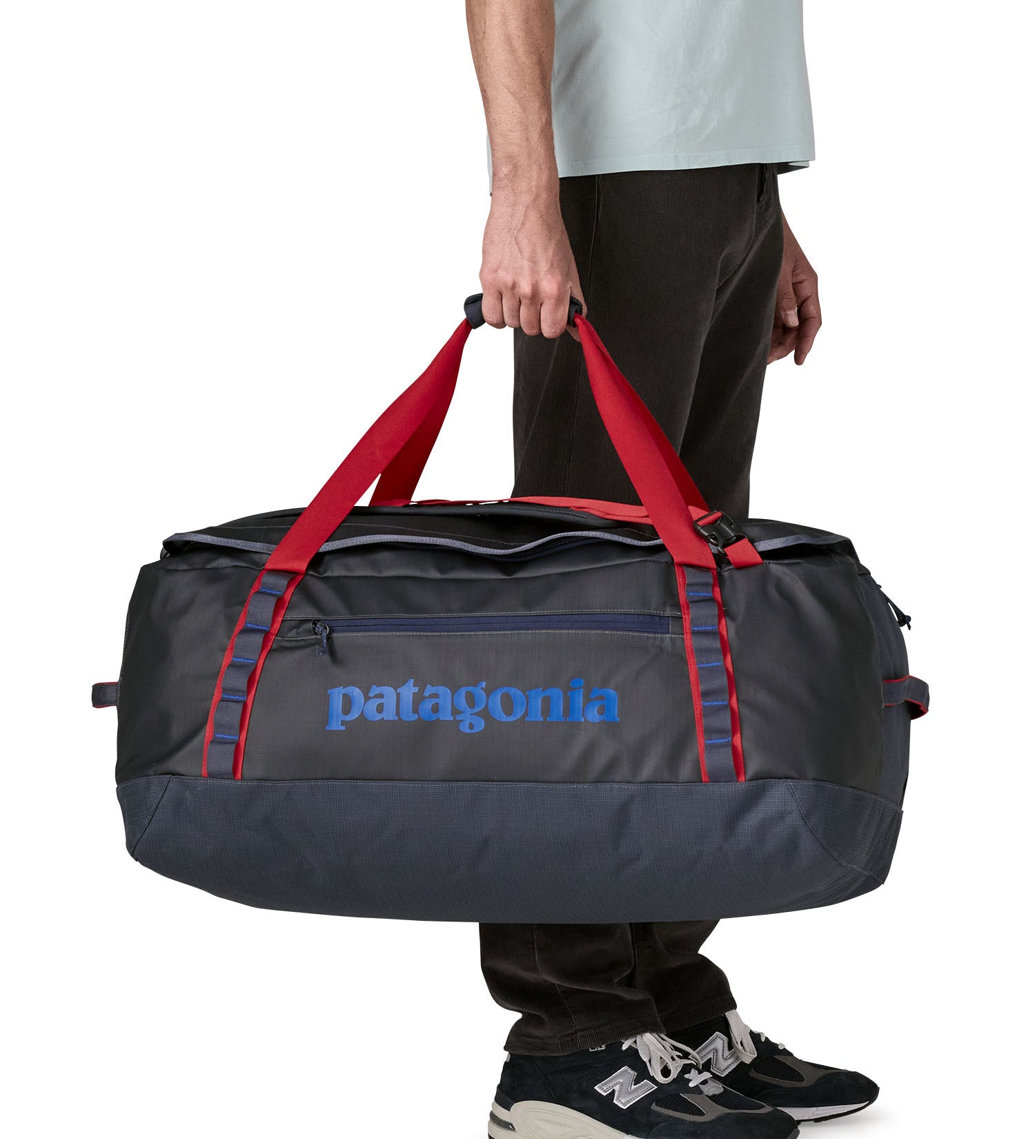 A man carrying the Patagonia black hole 70L duffel bag in smolder blue / amanita red available at Babipur. 