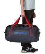 A man carrying the Patagonia black hole 70L duffel bag in smolder blue / amanita red available at Babipur. 