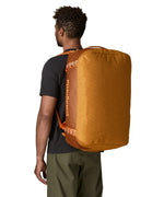 Back of man carrying the Patagonia black hole 55L duffel bag in Cinnamon brown showing the protective panel on the underside of the bag