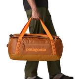 Side of man carrying the Patagonia black hole 55L duffel bag in Cinnamon brown using the carry handles 