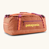 Patagonia black hole 55l duffel bag in bright orange with purple zip details, straps and yellow printed logo on front panel 