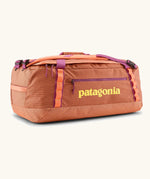 Patagonia black hole 55l duffel bag in bright orange with purple zip details, straps and yellow printed logo on front panel 