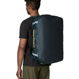 Back of man carrying the Patagonia black hole 55L duffel bag in dark teal on their shoulder showing the protective panel on the underside of the bag