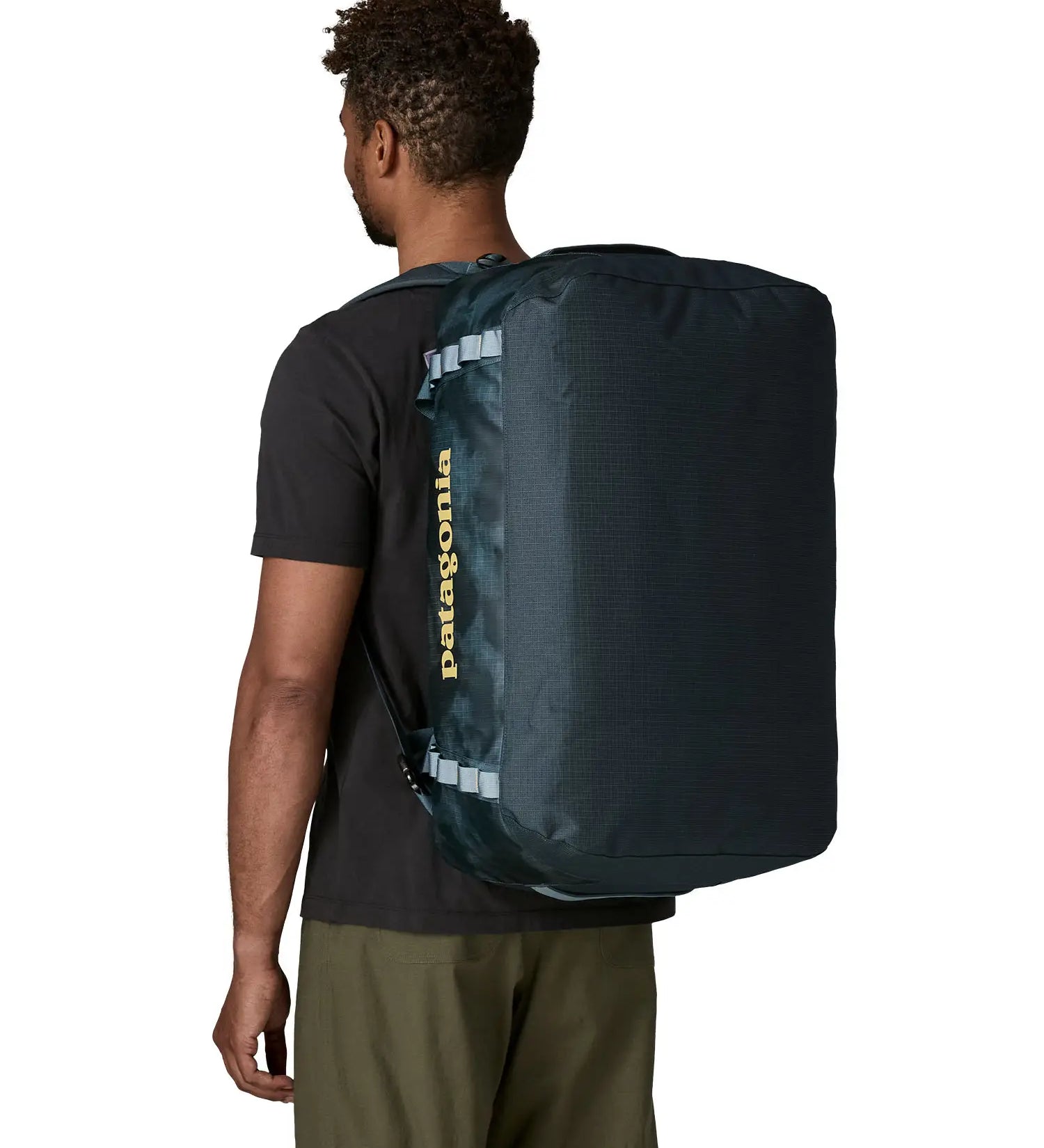 Back of man carrying the Patagonia black hole 55L duffel bag in dark teal on their shoulder showing the protective panel on the underside of the bag