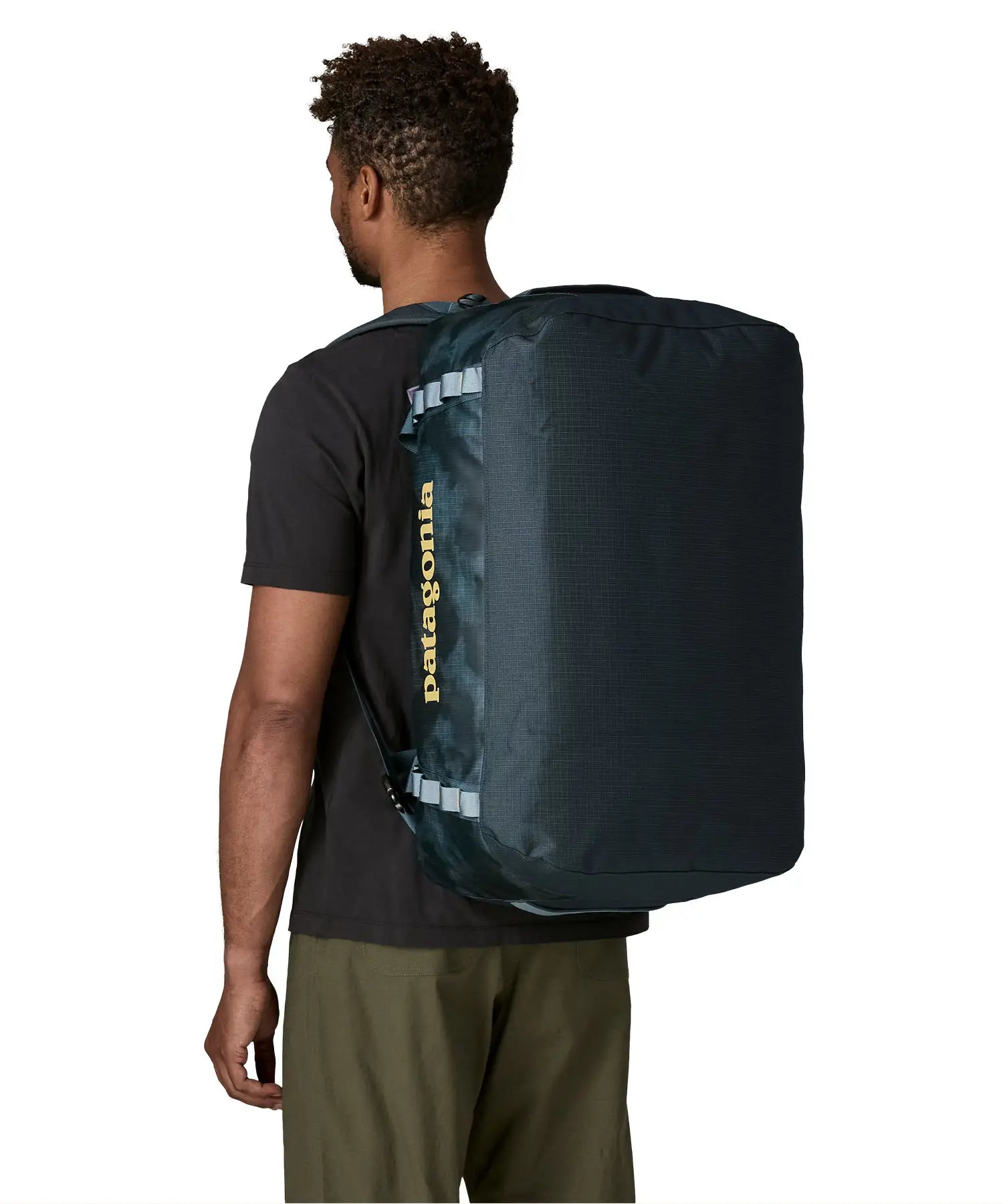 Back of man carrying the Patagonia black hole 55L duffel bag in dark teal on their shoulder showing the protective panel on the underside of the bag