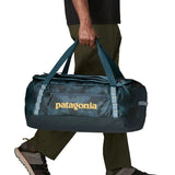 Side of man carrying the Patagonia black hole 55L duffel bag in dark teal using the carry handles 