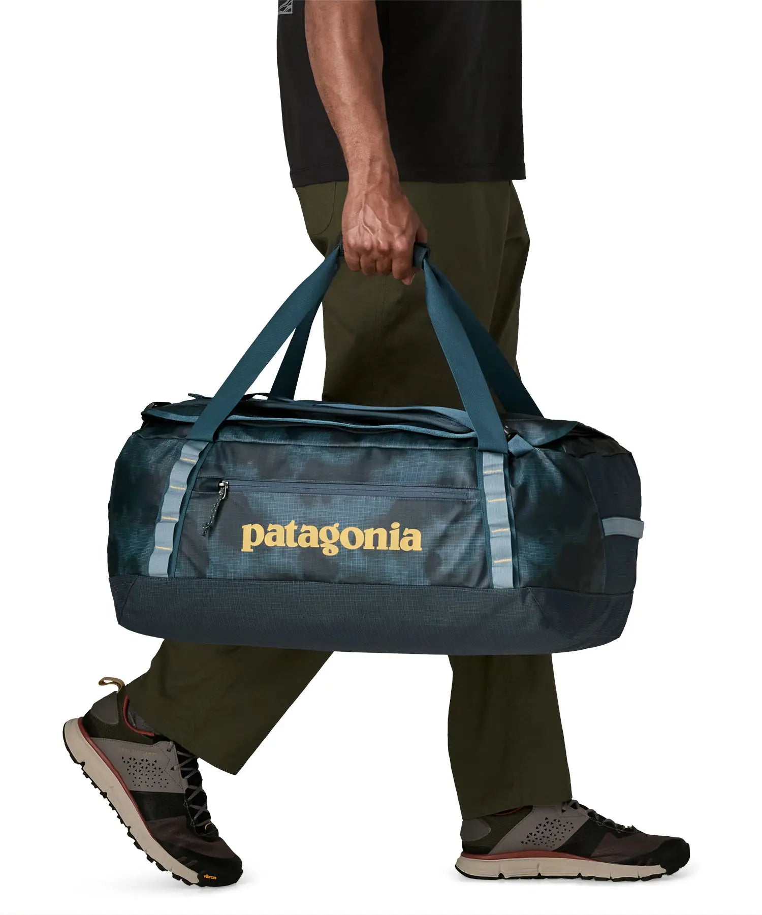 Side of man carrying the Patagonia black hole 55L duffel bag in dark teal using the carry handles 
