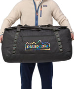 A person holding the Patagonia Black Hole Duffel 100L Ink Black in their hands, showing the size