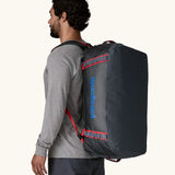 Man carrying Patagonia black hole duffle 55L in smolder blue w/ red on his back using shoulder straps.