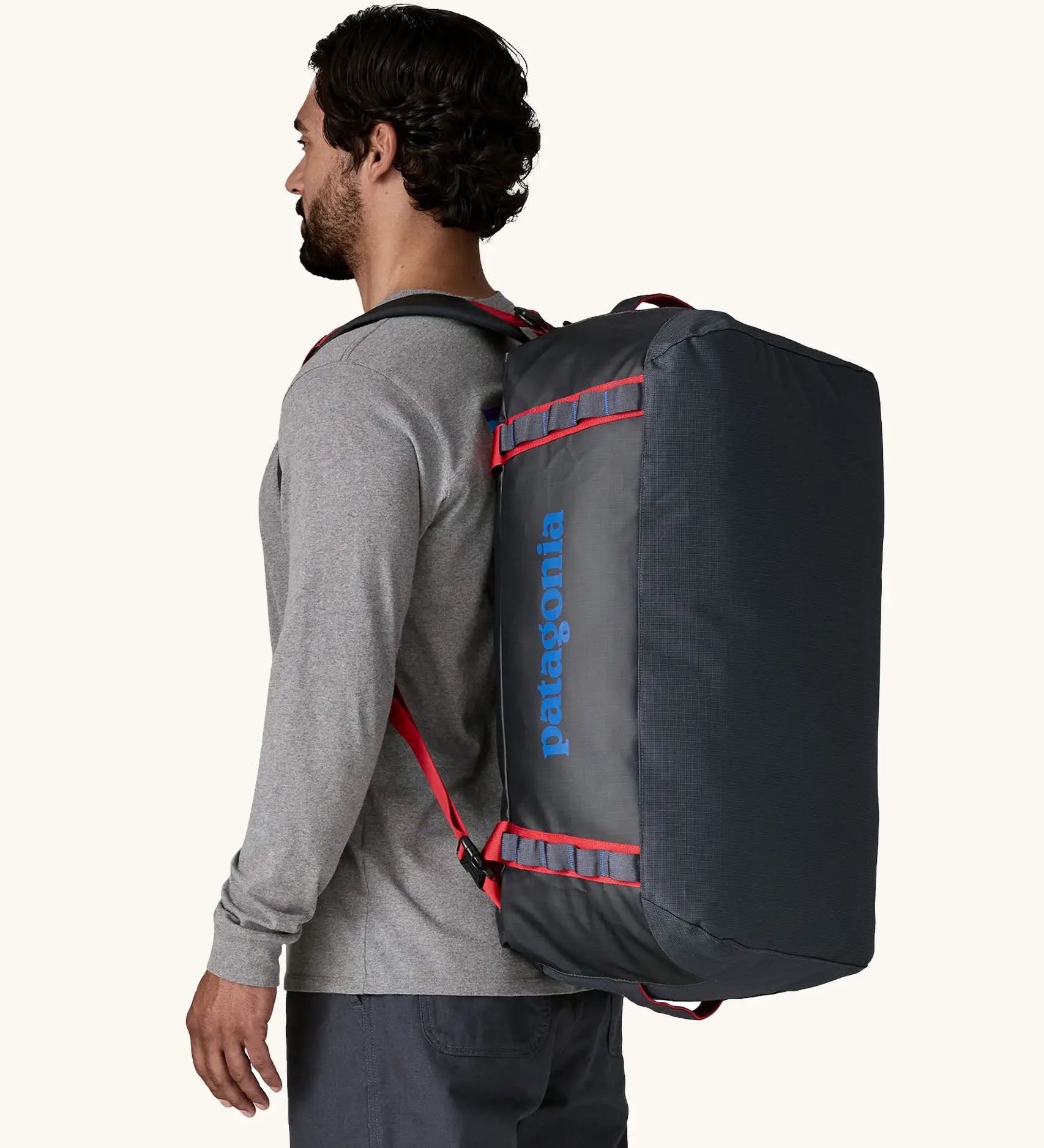 Man carrying Patagonia black hole duffle 55L in smolder blue w/ red on his back using shoulder straps.
