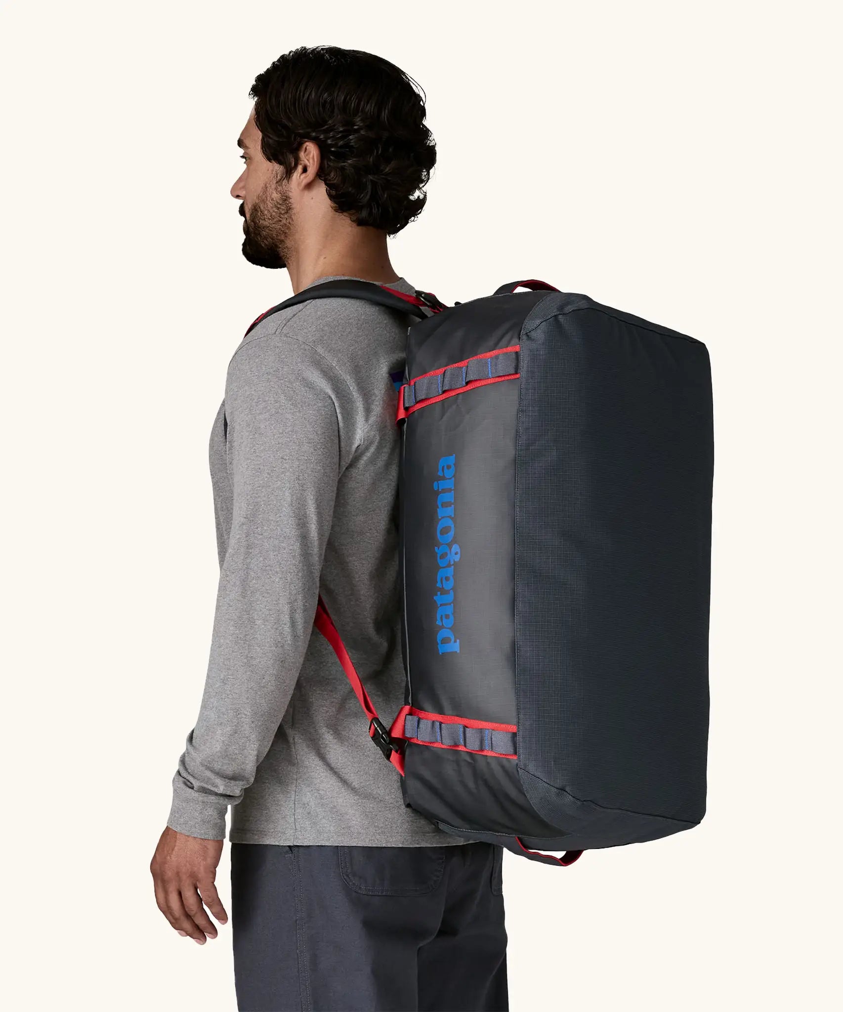 Man carrying Patagonia black hole duffle 55L in smolder blue w/ red on his back using shoulder straps.