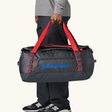 Man holding Patagonia black hole duffle 55L in smolder blue w/red using handle straps. 
