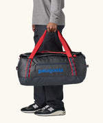 Man holding Patagonia black hole duffle 55L in smolder blue w/red using handle straps. 