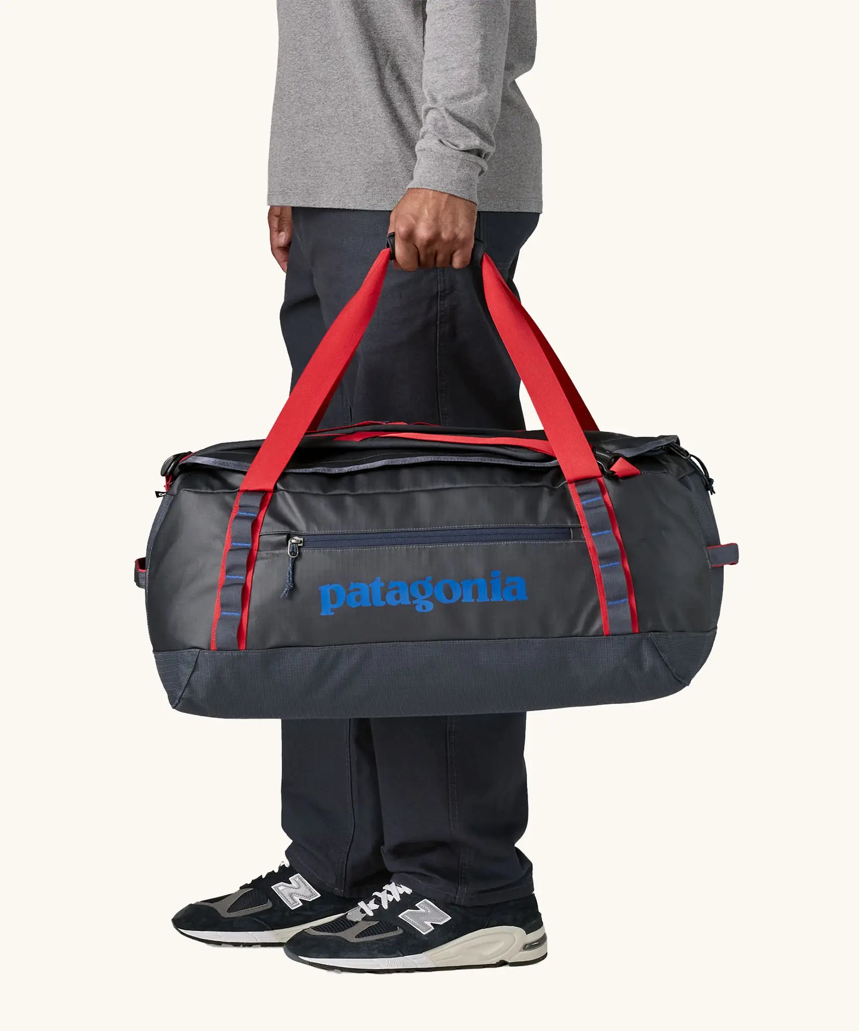 Man holding Patagonia black hole duffle 55L in smolder blue w/red using handle straps. 