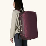 Woman carrying Patagonia black hole duffle 70L in berry fig on her back using shoulder straps. 