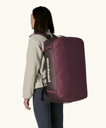 Woman carrying Patagonia black hole duffle 70L in berry fig on her back using shoulder straps. 