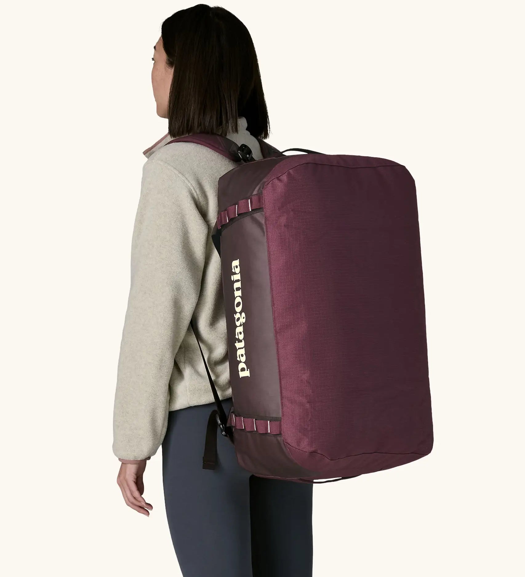 Woman carrying Patagonia black hole duffle 70L in berry fig on her back using shoulder straps. 