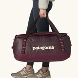 Woman carrying Patagonia black hole duffle 70L in berry fig using handle straps. 