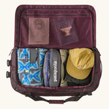 Patagonia Black Hole duffle 70L in berry fig, open to show storage space and zipped mesh pocket. 