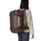 An adult carrying a  Patagonia 45 litre black hole travel backpack in maroon using the shoulder and hip straps