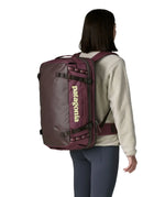 An adult carrying a  Patagonia 45 litre black hole travel backpack in maroon using the shoulder and hip straps