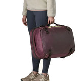 An adult carrying a Patagonia 45 litre black hole travel backpack in maroon using the carry strap on the side