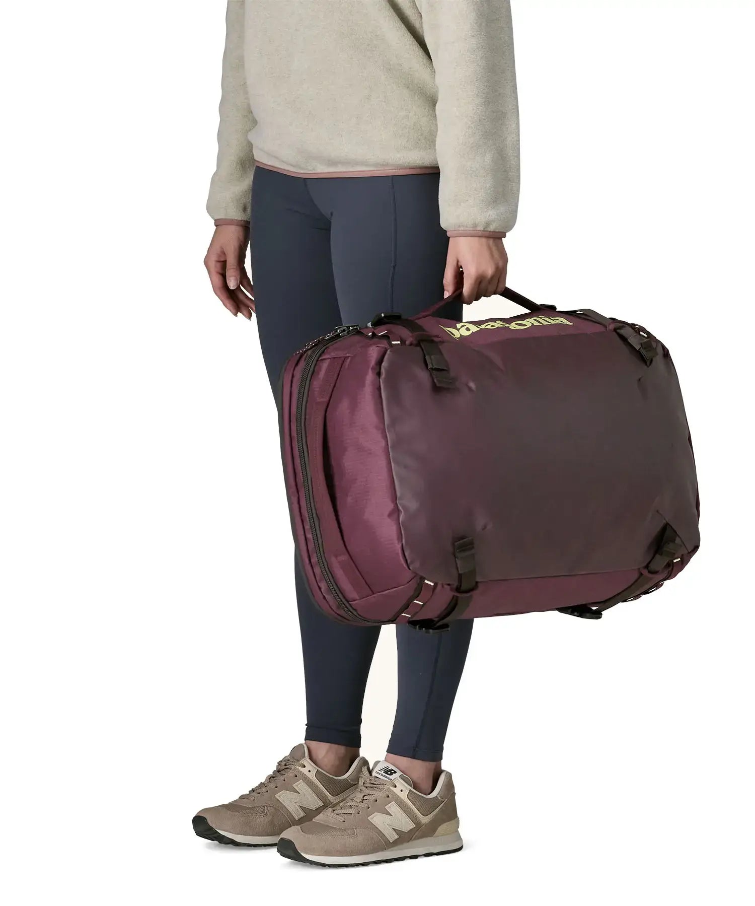 An adult carrying a Patagonia 45 litre black hole travel backpack in maroon using the carry strap on the side