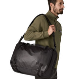 An adult carrying a Patagonia 45 litre black hole travel backpack in all black  over the shoulder with the crossbody strap