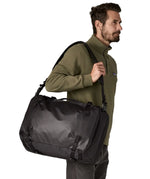 An adult carrying a Patagonia 45 litre black hole travel backpack in all black  over the shoulder with the crossbody strap