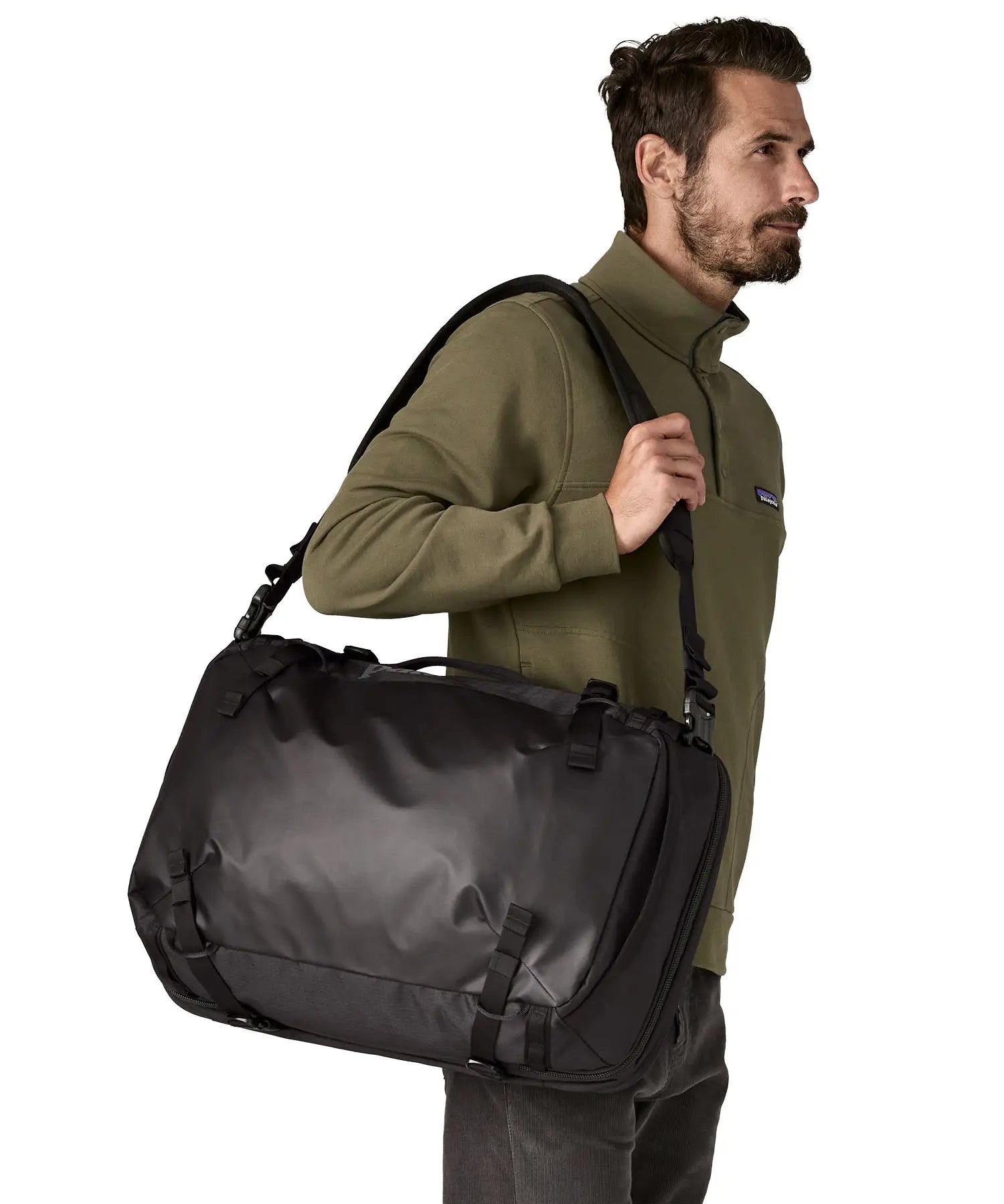 An adult carrying a Patagonia 45 litre black hole travel backpack in all black  over the shoulder with the crossbody strap