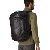An adult carrying a Patagonia 45 litre black hole travel backpack in all black using the shoulder and hip straps