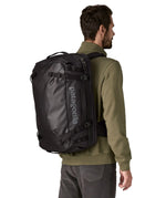 An adult carrying a Patagonia 45 litre black hole travel backpack in all black using the shoulder and hip straps