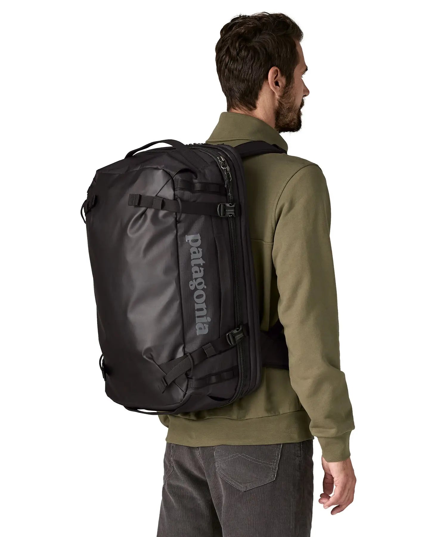 An adult carrying a Patagonia 45 litre black hole travel backpack in all black using the shoulder and hip straps