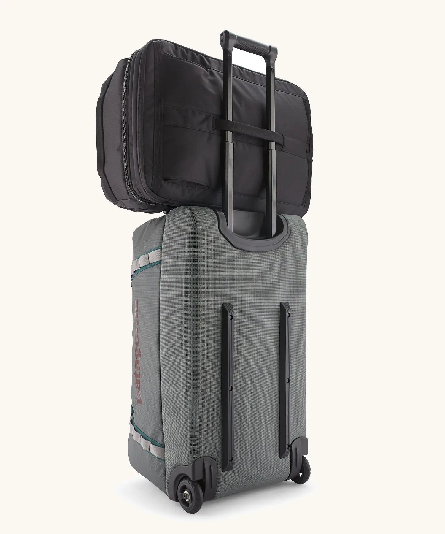 Patagonia 45 litre black hole weather resistant travel backpack in all black on top of a wheeled duffel bag through a loop on the back