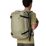 An adult carrying a Patagonia 45 litre black hole travel backpack in beige using the shoulder and hip straps