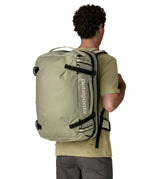 An adult carrying a Patagonia 45 litre black hole travel backpack in beige using the shoulder and hip straps