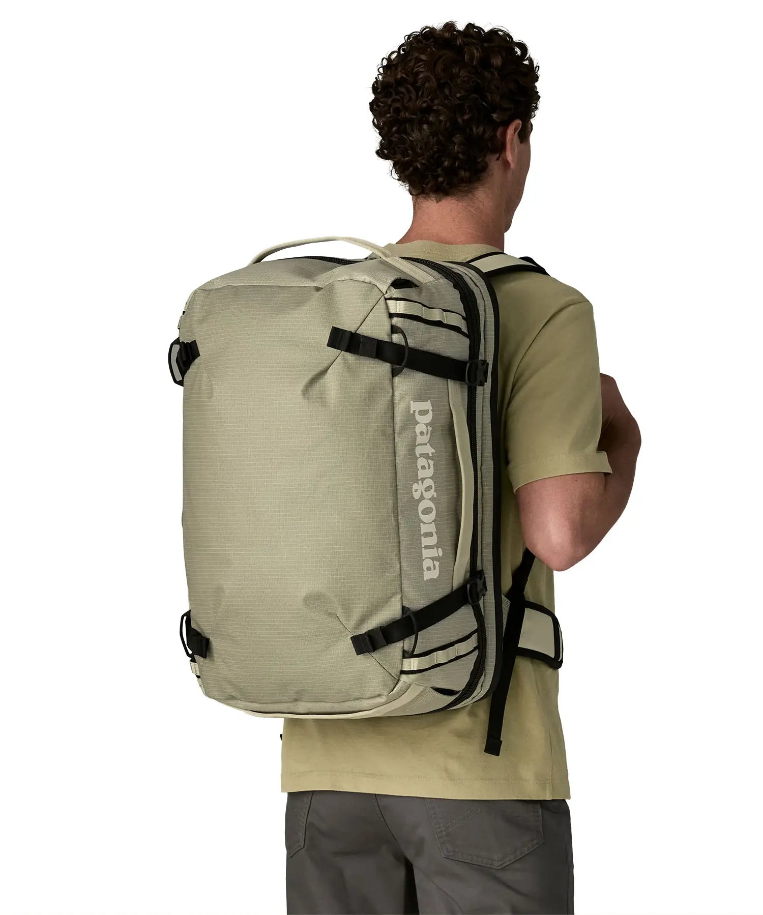 An adult carrying a Patagonia 45 litre black hole travel backpack in beige using the shoulder and hip straps