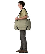 An adult carrying a Patagonia 45 litre black hole travel backpack in beige over the shoulder using the crossbody strap