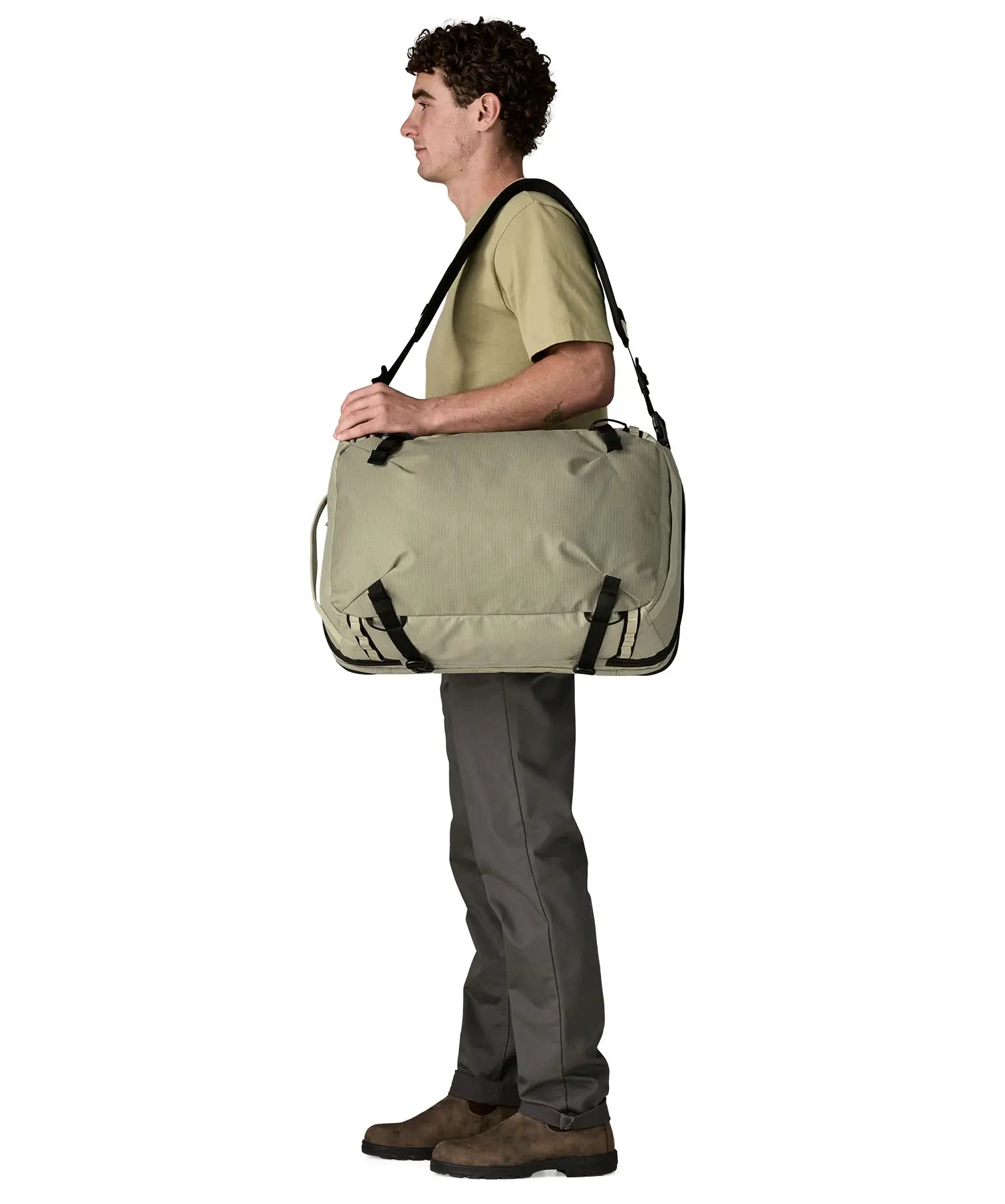 An adult carrying a Patagonia 45 litre black hole travel backpack in beige over the shoulder using the crossbody strap