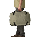 Side of an adult carrying a Patagonia 45 litre black hole travel backpack in beige over the shoulder using the carry handle 