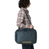 Woman carrying a Patagonia 22 litre black hole micro travel backpack in teal using the crossbody strap