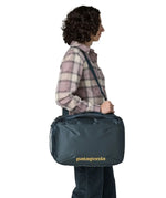 Woman carrying a Patagonia 22 litre black hole micro travel backpack in teal using the crossbody strap