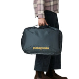 Woman carrying a Patagonia 22 litre black hole micro travel backpack in teal by the carry handle on the side