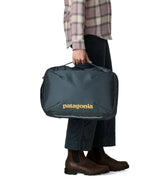 Woman carrying a Patagonia 22 litre black hole micro travel backpack in teal by the carry handle on the side