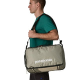 Man carrying a Patagonia 30 litre black hole travel backpack in beige over the shoulder using the crossbody strap