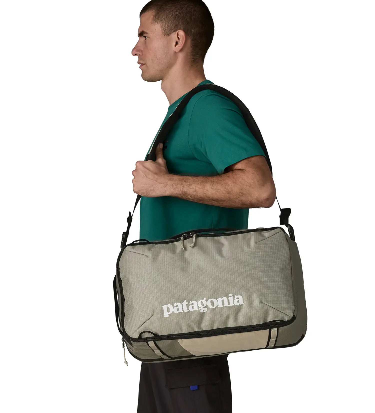 Man carrying a Patagonia 30 litre black hole travel backpack in beige over the shoulder using the crossbody strap