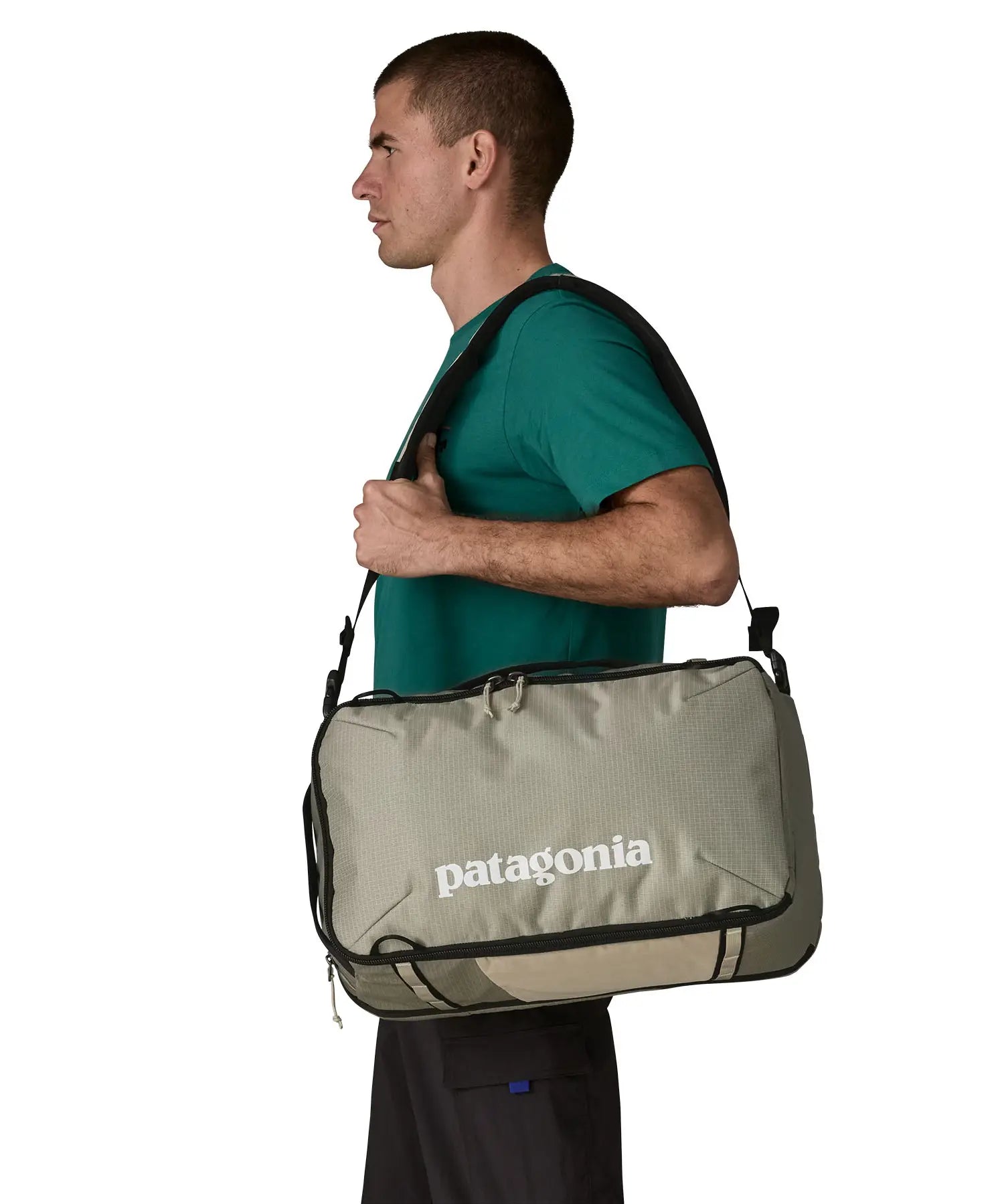 Man carrying a Patagonia 30 litre black hole travel backpack in beige over the shoulder using the crossbody strap